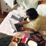 바쁜 직장인, 작은 변화로 건강 챙기기…“책상 앞 루틴이 답이다” Woman working on laptop on bed with snacks and books.