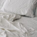 수면의 질 높이는 생활 습관 변화, 실천이 답이다 A rumpled white duvet and pillows on a bed.