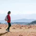 “저녁 산책, 달라지는 일상: 작은 움직임이 주는 큰 변화” a man with a backpack walking across a dry grass covered field